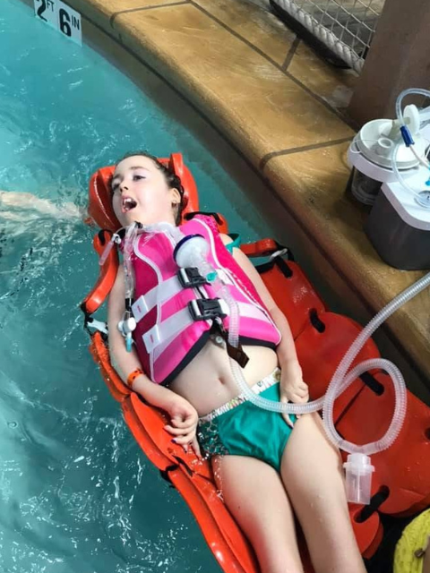 Kennedy floating in a pool with a pink life jacket on.
