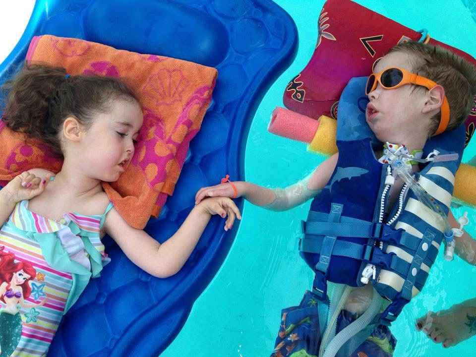 Two disabled children hold hands while floating in the pool.