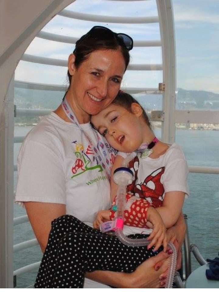 Jennifer Swann holding a young Kennedy in her arms. Both are smiling, with a view of the ocean out the window behind them.