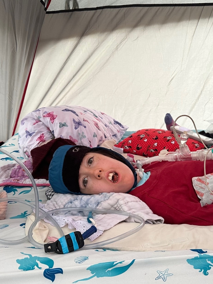 Kennedy laying in a tent on a camping trip, wearing a warm hat.
