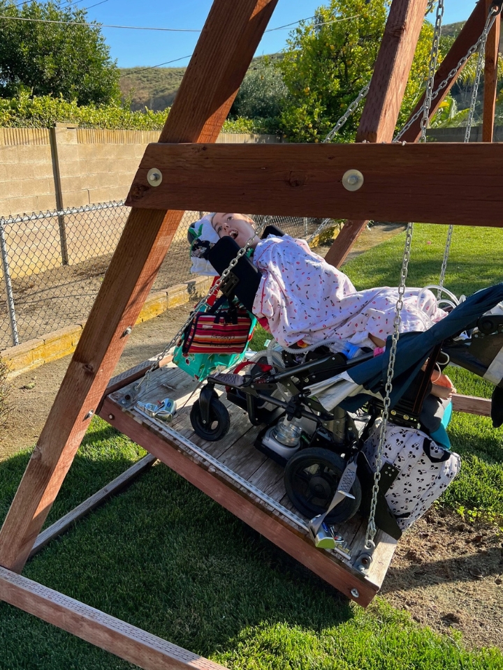 Kennedy on a sunny day on a swing set that accommodates her wheelchair.