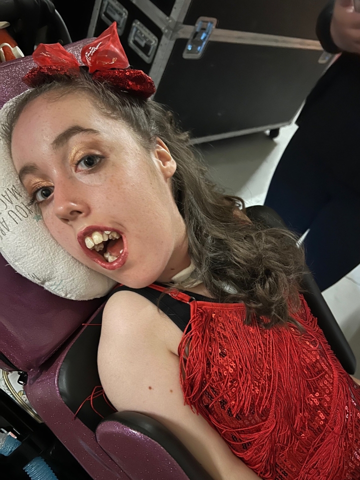 Kennedy reclined in her wheelchair, smiling and wearing a red dress.