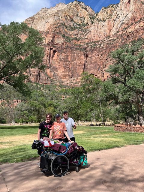 The Swann family smiling at Zion National Park with large red rocks and lush trees in the background.