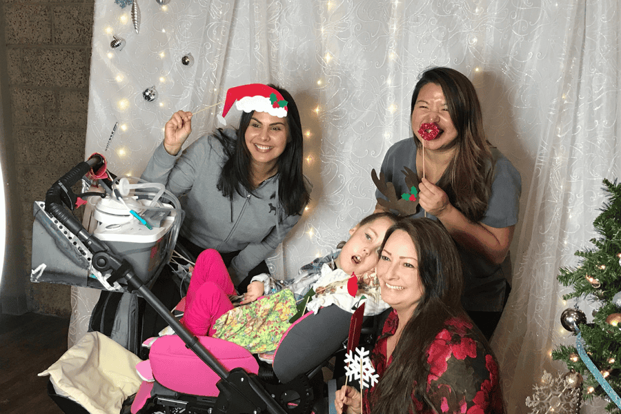 Care team posing with Kennedy at a holiday photo booth with festive props.