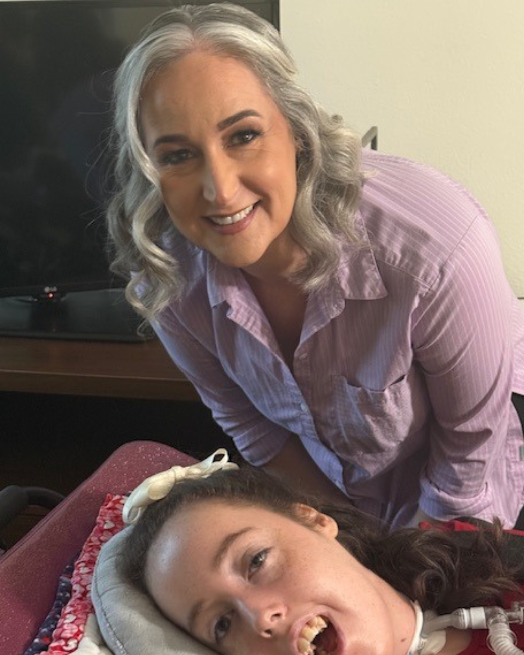 Jennifer in a lavender shirt smiling while leaning over Kennedy resting in a purple wheelchair.