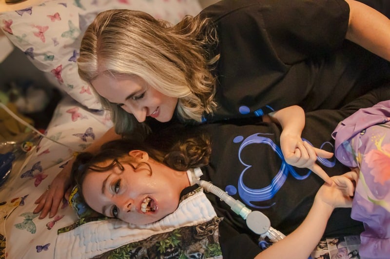 Woman lying beside a child with a medical device, both sharing a close and caring moment.
